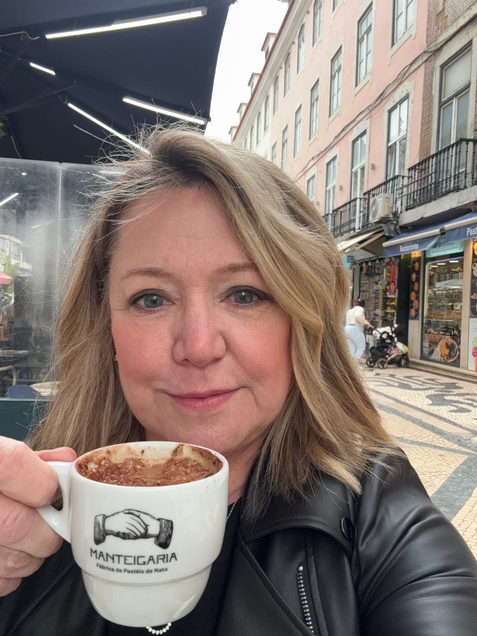 Michelle Haslam holding a cappuccino from Manteigaria, Fábrica de Pastéis de Nata, at a café in Lisbon, Portugal.