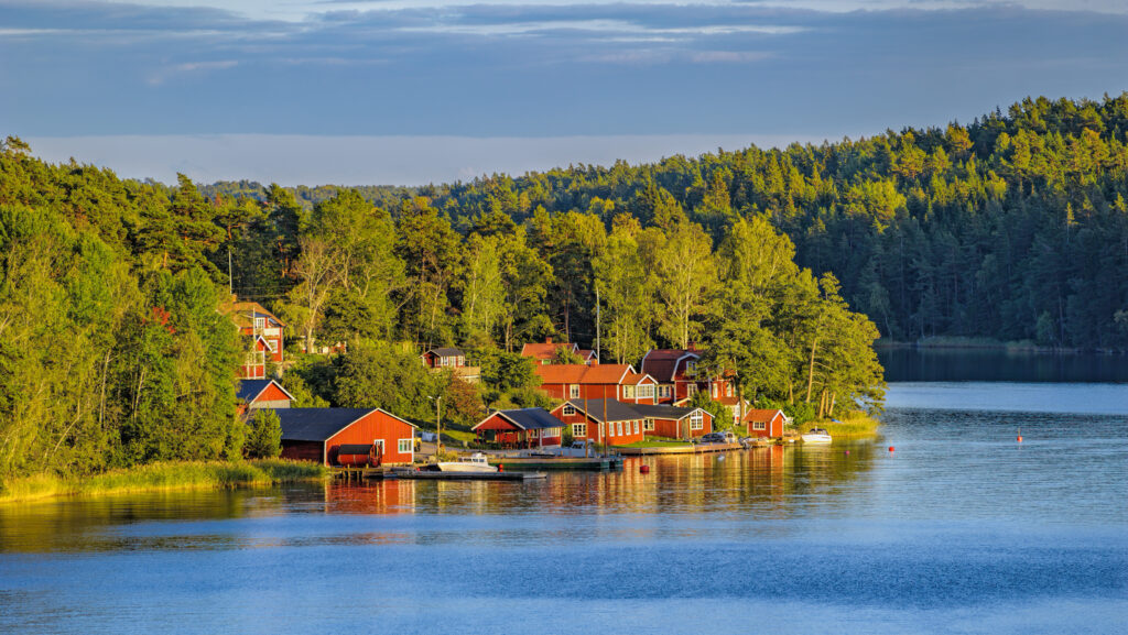 Red wooden cottages along the waterfront of a small island village in the Swedish archipelago at golden hour.