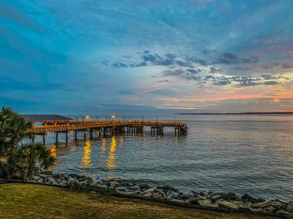 Golden afternoon light over a St Simons Island pier, with pier lights reflected in still tidal water