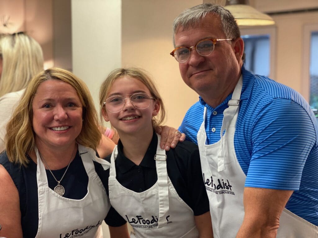 Grandparents and granddaughter wearing aprons together during a cooking class.
