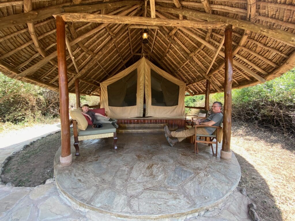 A grandfather and grandson relaxing under a thatched banda at a safari tented camp in Kenya during the midday downtime.